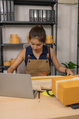 Genç bayan girişimci, ev ofisinden kıyafet satmak için yaşarken gülümsüyor. Moda ürünleri sunar, izleyicilerle iletişim kurar ve canlı seans sırasında online mağazasını yönetir..