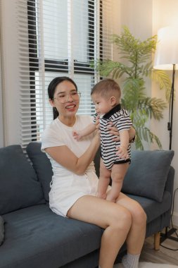 Genç bir anne, bebeğini sevgiyle kucaklar ve bir kanepede emzirir. Erken çocukluk ve aile hayatının anne bakımını, bağlarını ve besleyici anlarını sembolize eder..