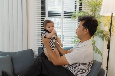 Bebeğini kucağında tutan bir babanın şefkatli anı. Bebek merakla ve güvenle yukarı bakıyor. Sıcak etkileşim aile sevgisini, yakınlaşmayı ve ebeveyn bakımını yansıtır..