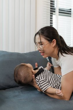 Bir anne bebeğiyle kanepede yatarken sevgi dolu bir şekilde iletişim kurar. Sıcak ve şefkatli bir an yaratır. Aile bağlarının güzelliğini yansıtır..
