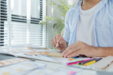 Odaklanmış bir tasarımcı UX / UI tasarım fikirleri üzerinde çalışıyor, bir tahtaya tutturulmuş renk paletleri ve arayüz yapılarını analiz ediyor. Sahne yaratıcılık, planlama ve dijital yeniliği yansıtıyor.