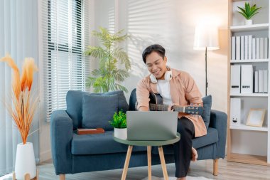 Genç bir adam oturma odasında zevkle gitar çalıyor, akor çalışırken ritmin tadını çıkarıyor. Rahat duruşu ve gülüşü mutluluğu ve müzikal tutkuyu yansıtıyor..