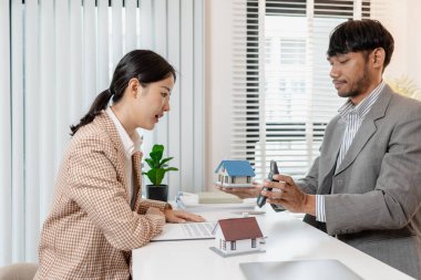 Bir emlakçı ve müşteri emlak satın alma seçeneklerini tartışıyor, sözleşmeyi gözden geçiriyor, kredi şartlarını hesaplıyor ve ev modellerini konut yatırımı kararının bir parçası olarak değerlendiriyor..