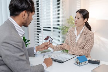 İki iş adamı emlak yatırımını tartışıyor, emlak sözleşmeleri imzalıyor ve ev modellerini gözden geçiriyor, konut satışlarını, finansmanı ve başarılı anlaşmaları sembolize ediyor.