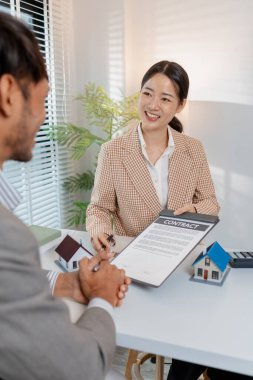 İki iş adamı emlak yatırımını tartışıyor, emlak sözleşmeleri imzalıyor ve ev modellerini gözden geçiriyor, konut satışlarını, finansmanı ve başarılı anlaşmaları sembolize ediyor.