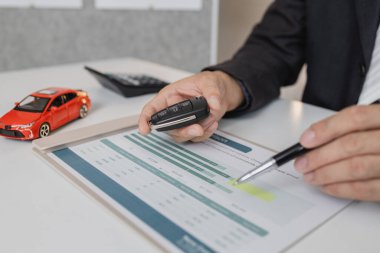 Takım elbiseli bir işadamı, hesap makinesi ve karşılaştırma çizelgesi kullanarak araç kredisi seçeneklerini hesaplıyor. Masasında model arabalar ve araba anahtarları bulunuyor. Finans, kiralama ve yatırım planlamasını sembolize ediyor..