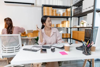 Küçük bir iş ofisinde birlikte çalışan iki genç kadın, çevrimiçi satış ve ambalaj siparişlerini yönetiyorlar. Biri mali raporları kontrol eder ve hesap makinesi kullanır, diğeri ise kutuları hazırlar..