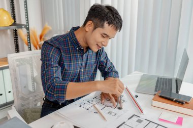 Ofis masasında çalışan kendinden emin genç mimar, ev planları çiziyor ve inşaat detaylarını telefonda tartışıyor, mimari tasarım ve proje planlamasında doğruluk ve yaratıcılığa odaklanıyor