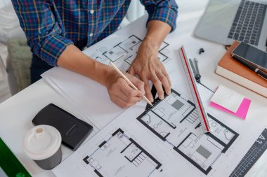 Genç bir erkek mimar masasında planlarla çalışıyor, cetvelleri kullanıyor ve detayları rafine etmek için aletler çiziyor. Odaklanmış ve meşgul görünüyor, yaratıcılığı hassasiyetle dengeliyor..