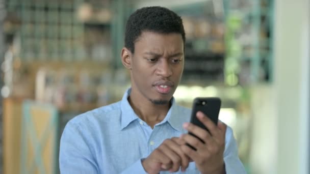 Porträt eines aufgebrachten jungen Afrikaners mit Verlust auf dem Smartphone — Stockvideo