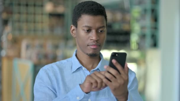 Porträtt av Positiv ung afrikansk man med hjälp av smartphone — Stockvideo