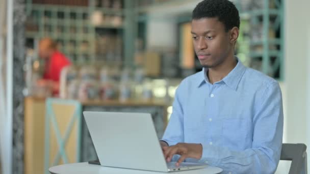 Ung afrikansk man med bärbar dator ler mot kameran i Café — Stockvideo