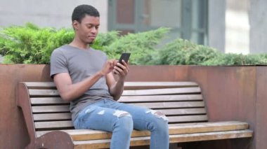 Dizüstü bilgisayarı olan genç bir Afrikalı Bench 'te Smartphone ile konuşuyor. 