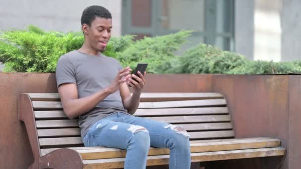 Homem africano jovem com dor nas costas usando laptop no banco — Vídeo de Stock