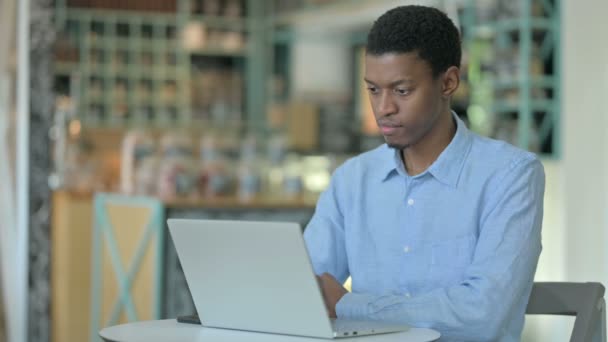 Pensativo joven africano hombre usando el ordenador portátil en Café — Vídeos de Stock