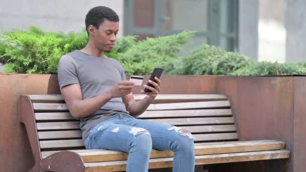 Rozzlobit mladý Afričan rozzlobený na Smartphone na lavičce — Stock video