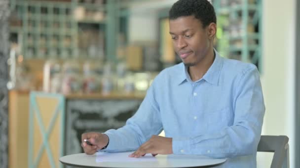En besviken ung afrikansk man som försöker skriva på papper — Stockvideo