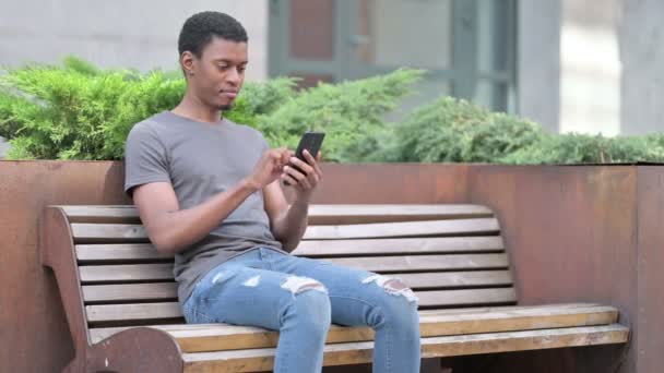 Mladý Afričan s notebookem mluví na Smartphone na lavičce — Stock video