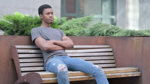 Młody Afrykanin siedzący na ławce i myślący — Wideo stockowe