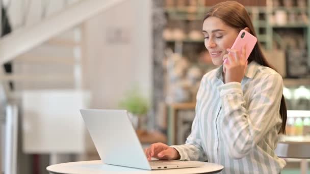 Mujer latina joven con el ordenador portátil hablando en el teléfono inteligente en Café — Vídeos de Stock