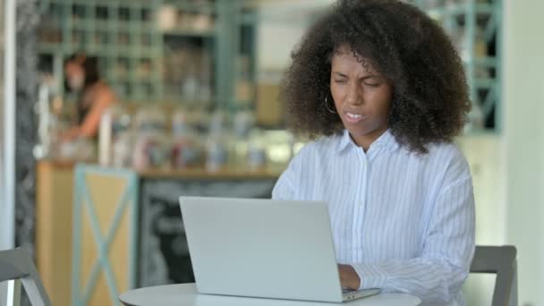 Mujer de negocios africana cansada con portátil que tiene dolor de espalda en el café — Vídeos de Stock