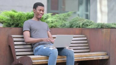 Neşeli Genç Afrikalı Adam Bench 'te dizüstü bilgisayardan video çağrısı yapıyor. 
