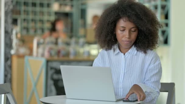 Afrikanische Geschäftsfrau mit Laptop spricht im Café mit Smartphone — Stockvideo