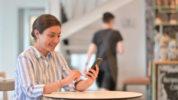 Excited Indian Woman Celebrating Success on Smartphone in Cafe — Stock Video