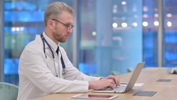 Орієнтований молодий чоловік лікар працює на ноутбуці в офісі — стокове відео