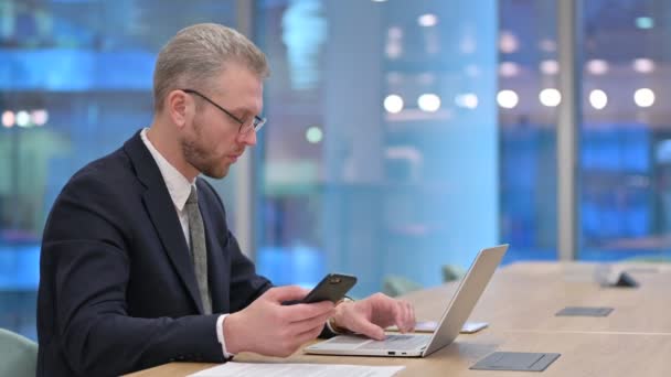 Profesjonalny młody biznesmen za pomocą smartfona i laptopa w biurze — Wideo stockowe