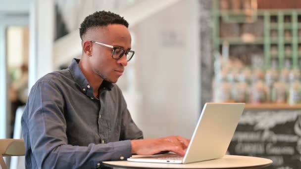 Atractivo hombre africano con ordenador portátil mirando a la cámara en Café — Vídeos de Stock