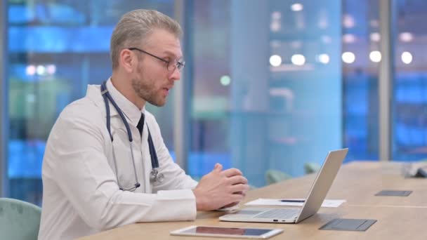 Профессиональный молодой врач делает видеозвонок на ноутбуке в офисе — стоковое видео