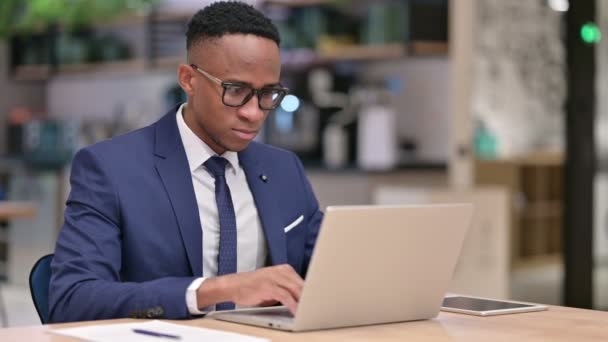 Ελκυστικός αφρικανός επιχειρηματίας με lap-top εξετάζοντας την κάμερα στο γραφείο — Αρχείο Βίντεο