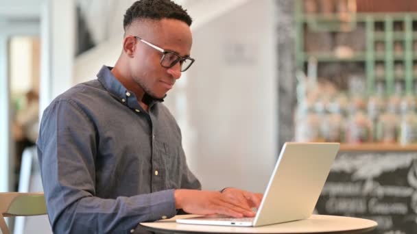 Joven africano con el ordenador portátil sonriendo en la cámara en Café — Vídeos de Stock