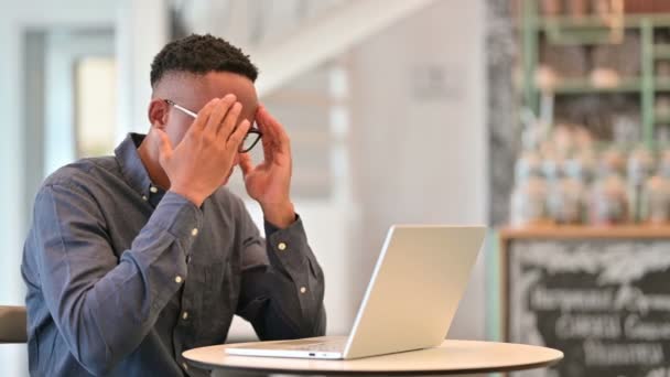 Hombre africano estresado con portátil con dolor de cabeza en Café — Vídeos de Stock