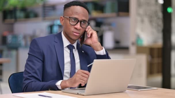 在办公室用智能手机与笔记本电脑交谈的非洲商人 — 图库视频影像