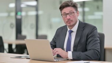 Bilgisayarlı orta yaşlı iş adamı kamerayı işaret ediyor. 