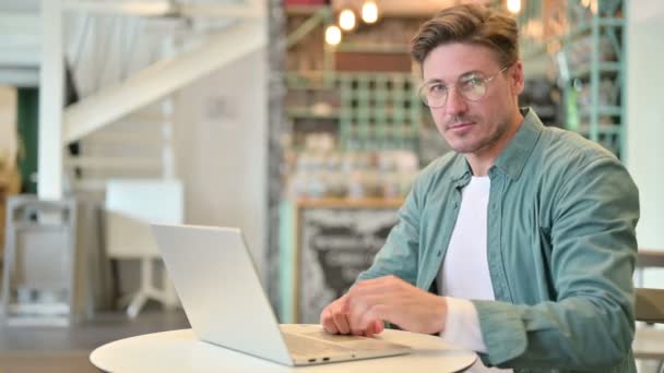 Hombre de mediana edad con el ordenador portátil señalando a la cámara en Café — Vídeo de stock