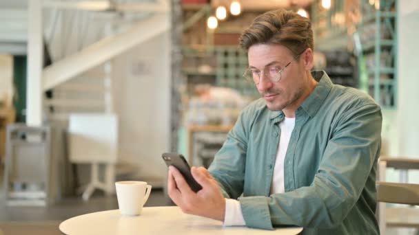 Hombre de mediana edad celebrando el éxito en el teléfono inteligente en Café — Vídeo de stock