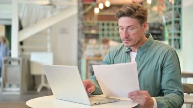 Cafe 'de dizüstü bilgisayarda ve belgelerde çalışan orta yaşlı bir adam.