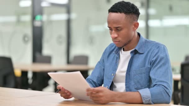 Hombre africano casual enfocado leyendo documentos en la oficina — Vídeo de stock