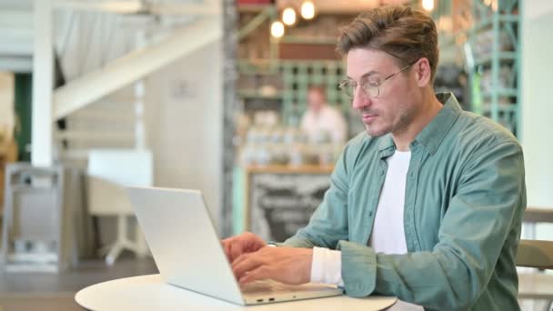 Hombre de mediana edad con el ordenador portátil sonriendo en la cámara en Café — Vídeos de Stock
