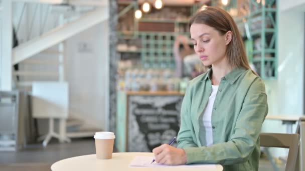 Vrouw denken en schrijven op papier in Cafe — Stockvideo