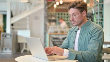 Laptop 'u olan orta yaşlı adam kafede sırt ağrısı çekiyor. 