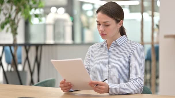 Молодая женщина испытывает шок, читая документы в офисе — стоковое видео
