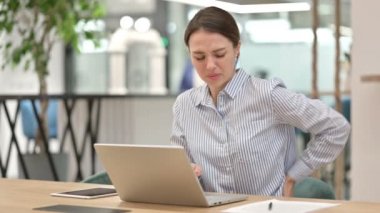 Dizüstü bilgisayarlı yorgun genç kadın ofiste sırt ağrısı çekiyor. 