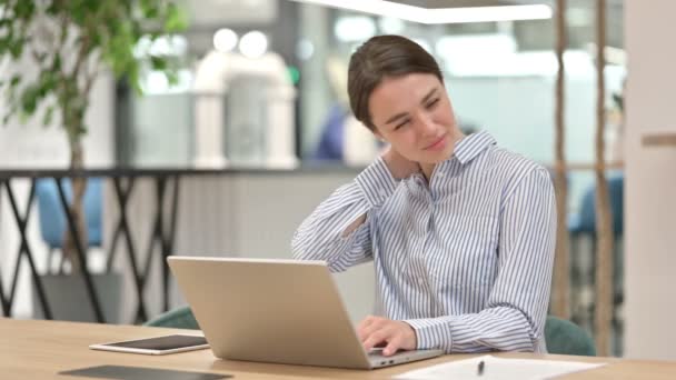 Уставшая молодая женщина с ноутбуком, имеющая боли в шее в офисе — стоковое видео