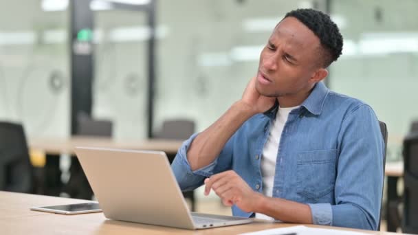 Casual Αφρικανικός άνθρωπος με φορητό υπολογιστή που έχει πόνο στο λαιμό στο γραφείο — Αρχείο Βίντεο