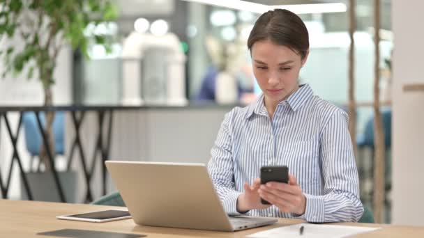 Jovem mulher profissional com laptop usando Smartphone no escritório — Vídeo de Stock