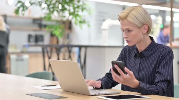 Seriös ung affärskvinna med Smartphone och laptop i Office — Stockvideo